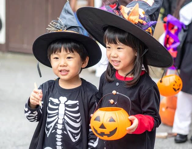 黒い魔女帽子で仮装した2人の子ども。かぼちゃのバケツを持って笑顔を見せている